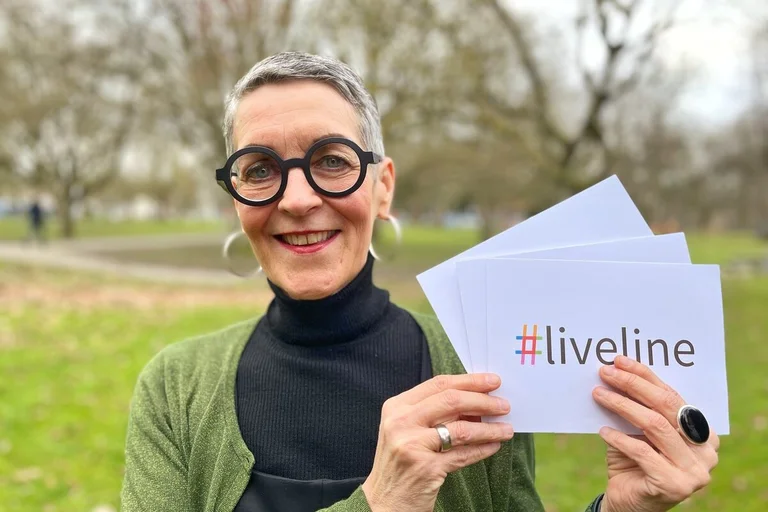 Eine Frau steht in einem Park und hält Karten in die Kamera. 