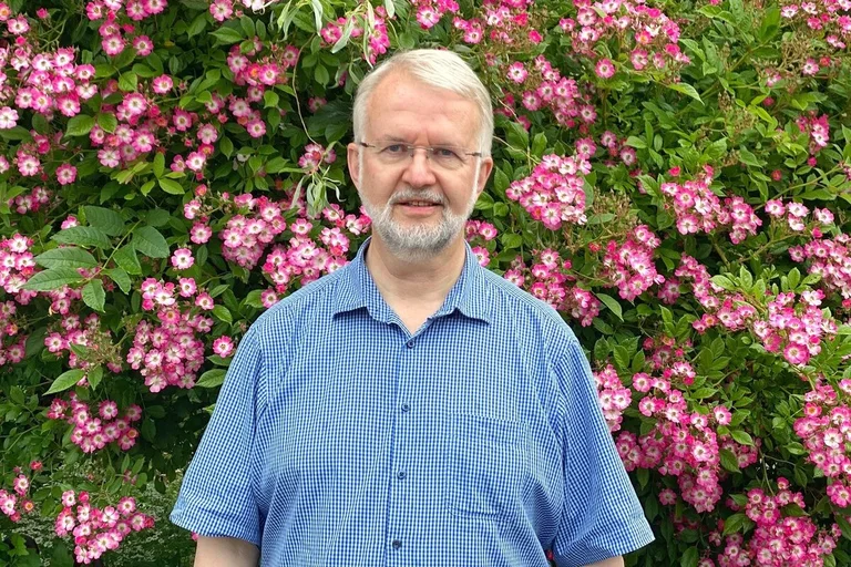 Ein Mann steht vor einer blühenden Hecke