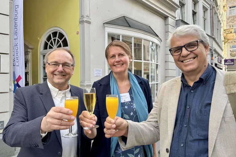 Drei Personen stoßen vor einem haus mit Getränken an. 