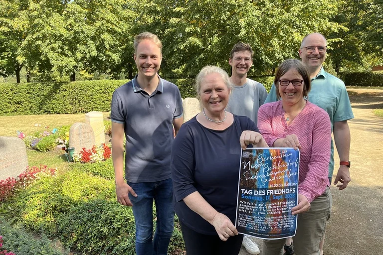 Drei Männer und zwei Frauen stehen auf einem Friedhof