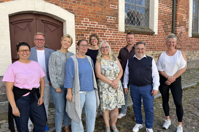 Neun Frauen und Männer stehen für ein Gruppenbild zusammen