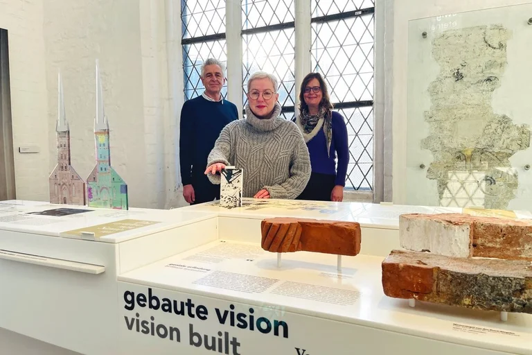 Drei Personen stehen hinter einem Tisch in einer Ausstellung