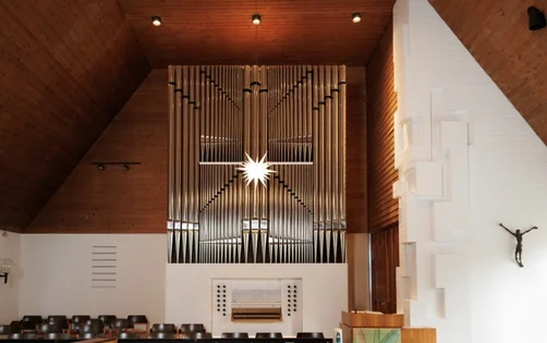 Innenraum einer Kirche, die Decke ist mit hellem Holz getäfelt, man sieht eine Orgel mit Orgelpfeifen