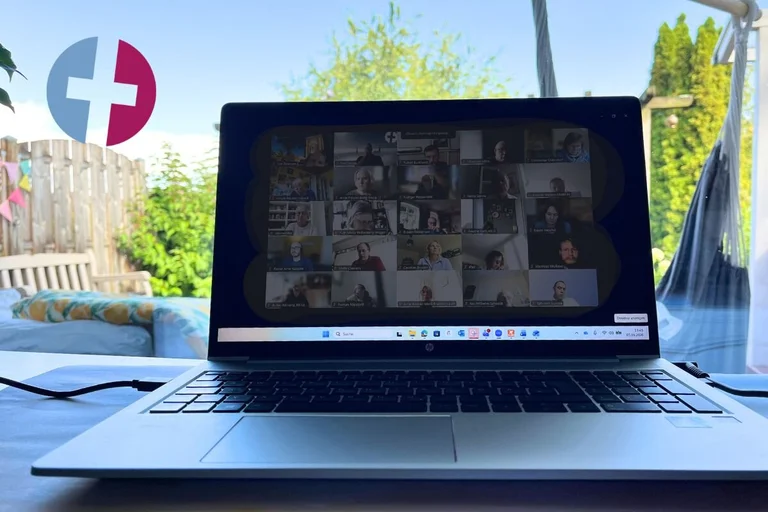 Ein Laptop steht auf einem Schreibtisch mit Garten und blauem Himmel im Hintergrund.