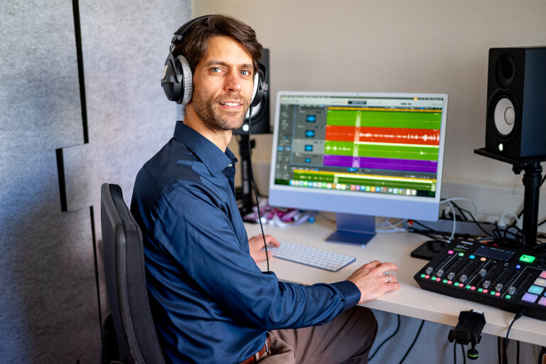 Ein Mann mit Kopfhörern sitzt an einem PC mit Mischpult und Audio-Schnittprogramm.