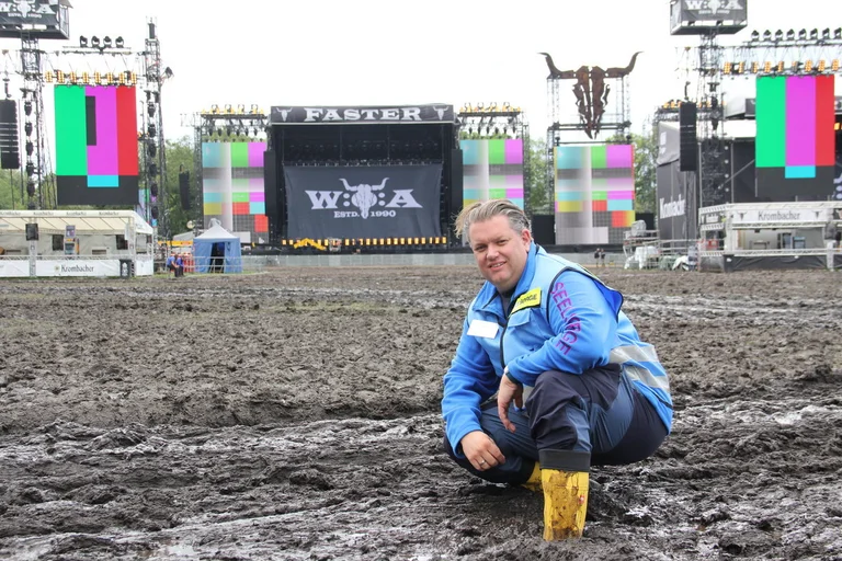 Ein Mann steht auf einer matschigen Wiese vor einer Konzertbühne