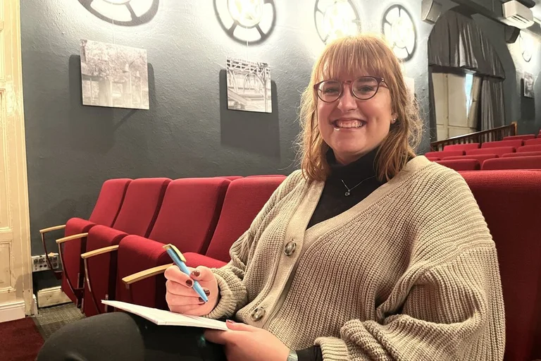 Eine Frau sitzt in einem Kino und lächelt in die Kamera. 