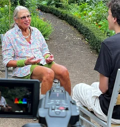 Eine Frau und ein Mann sitzen auf Gartenstühlen und eine Kamera ist im Bild