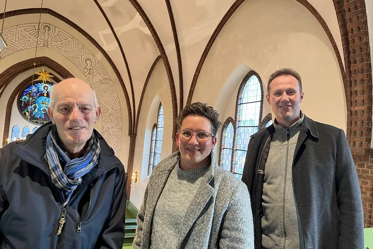Drei Menschen in der Kirche blicken den Fotografen an.