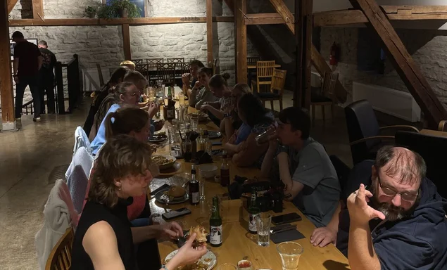 Menschen sitzen an einem einem langen Holztisch und essen
