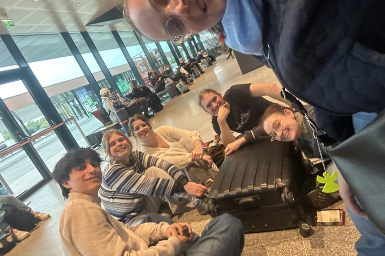 Junge Menschen sitzen mit ihren Koffern auf dem Flughafenboden.