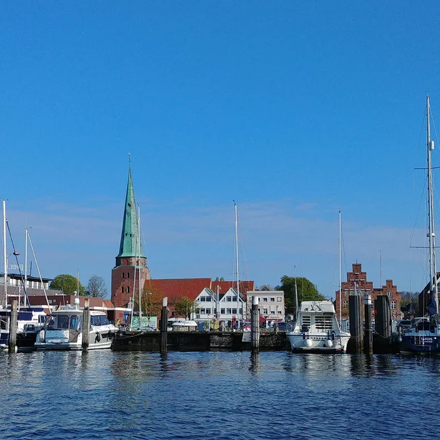 Eine Kirche am Wasser, davor Motorboote und Seegelboote