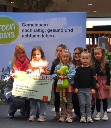 Eine Gruppe von Kleinkindern steht zusammen mit Erzieherinnen auf einer Bühne und hält einen großen Pappcheck.