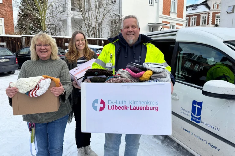 Drei Personen stehen mit Kartons vor einem Auto 