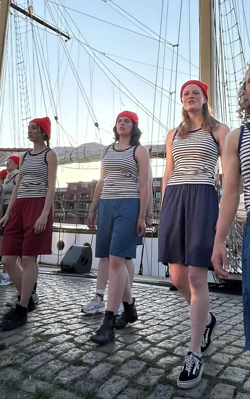 Junge Menschen in Matrosenkleidung vor einem Segelschiff.