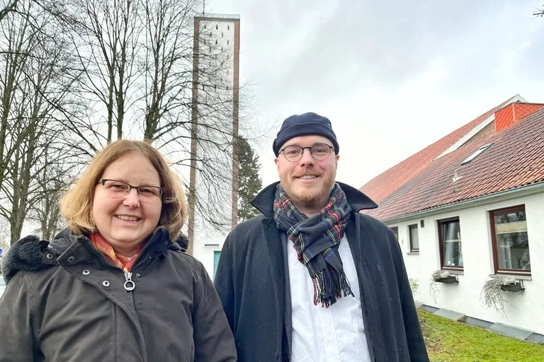 Zwei Personen vor einer Kirche im Winter.