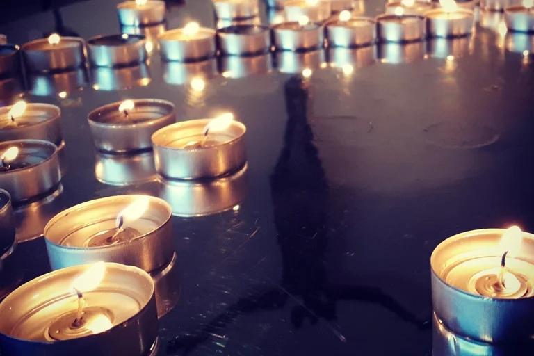 Brennende Teelichte auf dem Tisch, auf der Tischplatte spiegelt sich das Anlitz Jesu.