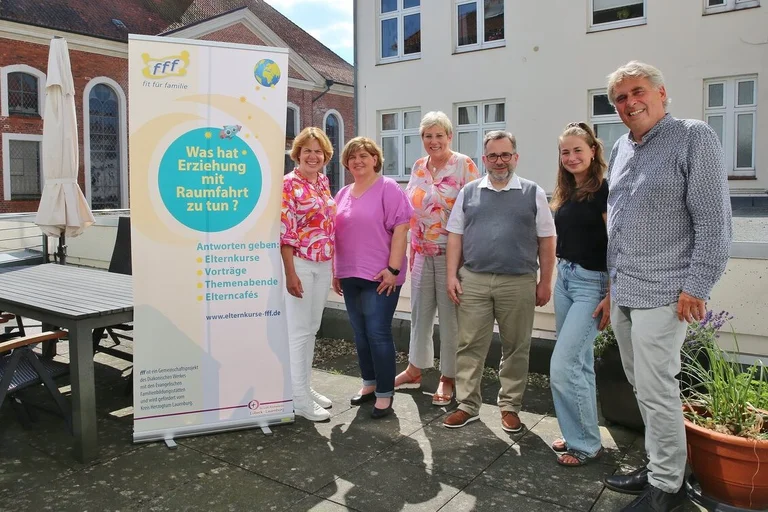 Mehrere Frauen und Männer stehen draußen neben einem hochformatigen Banner.