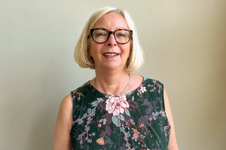 Eine Frau mit grauen kinnlangen Haaren und Brille lächelt in die Kamera.