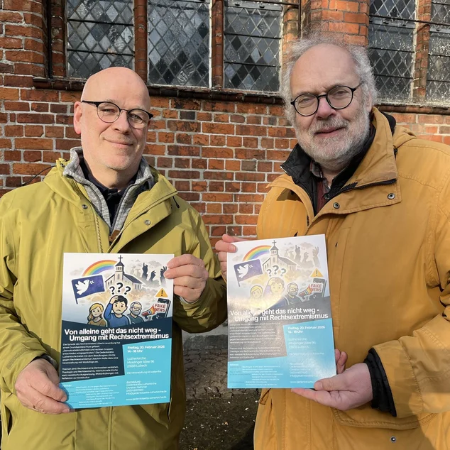 Zwei Männer in hellen Jacken halten zwei Plakate in die Kamera.