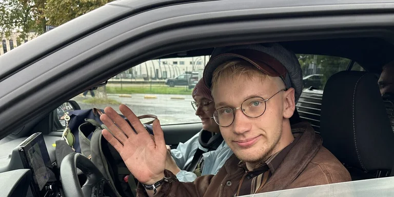 Ein junger Mann winkt aus einem Auto