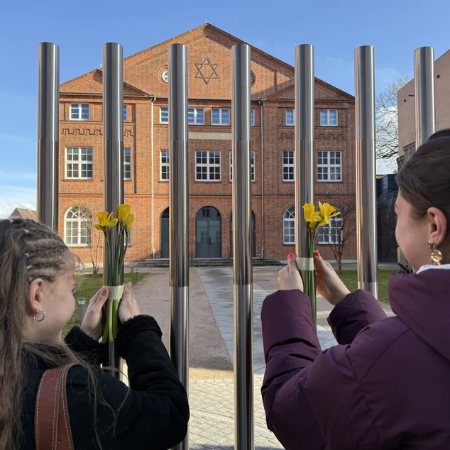 Zwei junge Frauen befestigen Blumen am Zaun einer Synagoge.
