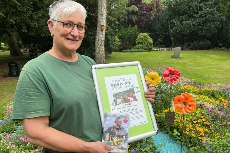 Eine Frau steht mit einem Plakat auf einem Friedhof.