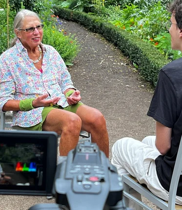 Eine Frau und ein Mann sitzen auf Gartenstühlen und eine Kamera ist im Bild