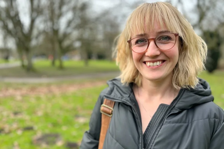 Eine Frau steht lächelnd in einem Park