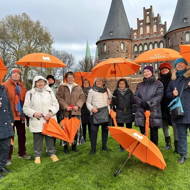 Eine Gruppe von Frauen steht mit orangenen Schirmen vor dem Holstentor. 