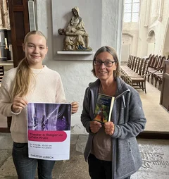Zwei Frauen stehen mit einem Plakat in einer Kirche.