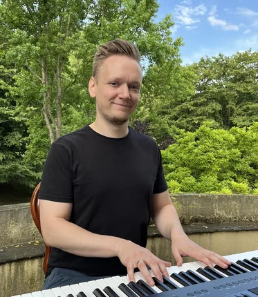 Ein junger Mann sitzt draußen im Grünen an einem Piano.