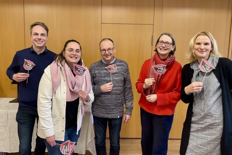 Fünf Männer und Frauen lächeln in die Kamera und halten Pappschilder vom Kirchentag.