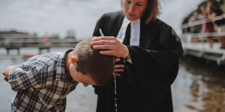 Eine Pastorin tauft einen Jungen im Wasser.