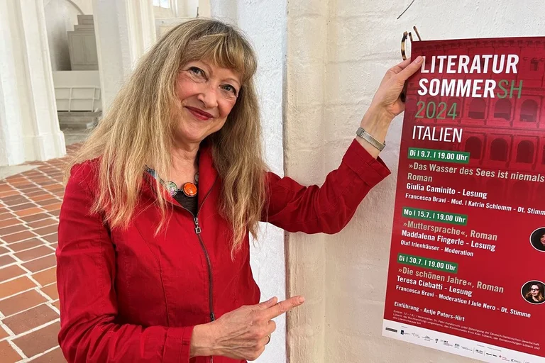 Eine Frau mit blonden Haaren zeigt auf ein Veranstaltungsplakat.