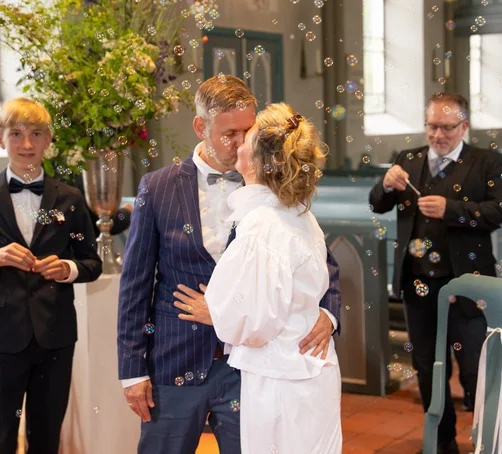 Ein Brautpaar küsst sich in einer Kirche inmitten von schwebenden Seifenblasen.