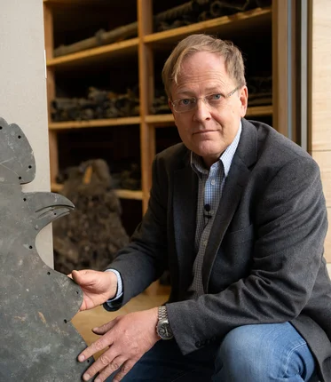 Ein Mann kniet neben einem Wetterhahn.