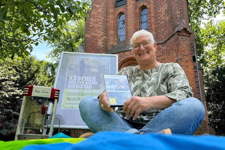 Frau sitzt auf einer Decke vor dem Glockenturm des St.-Lorenz-Friedhofes
