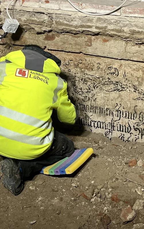 Eine Person mit gelber Warnweste arbeitet an einer Inschrift in einer Ausgrabungsstelle.