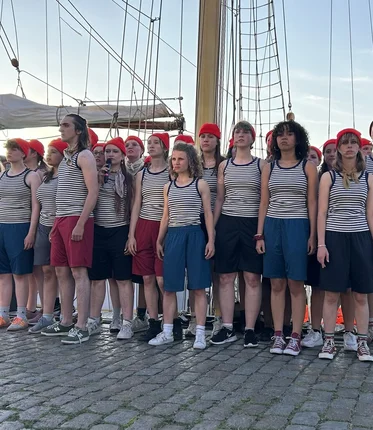 Eine Gruppe junger Menschen steht eng zusammen vor einem Segelschiff.