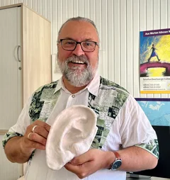 Mann steht mit Gipsohr in der Hand da und lächelt in die Kamera.