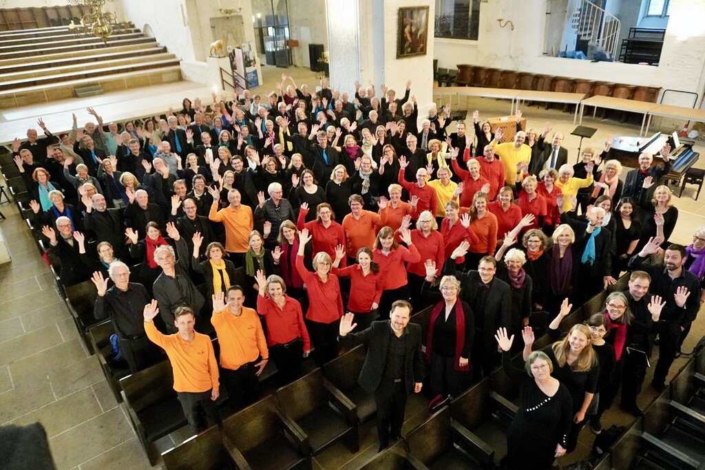 Ein großer Chor in einer Kirche von oben fotografiert winkt in die Kamera.