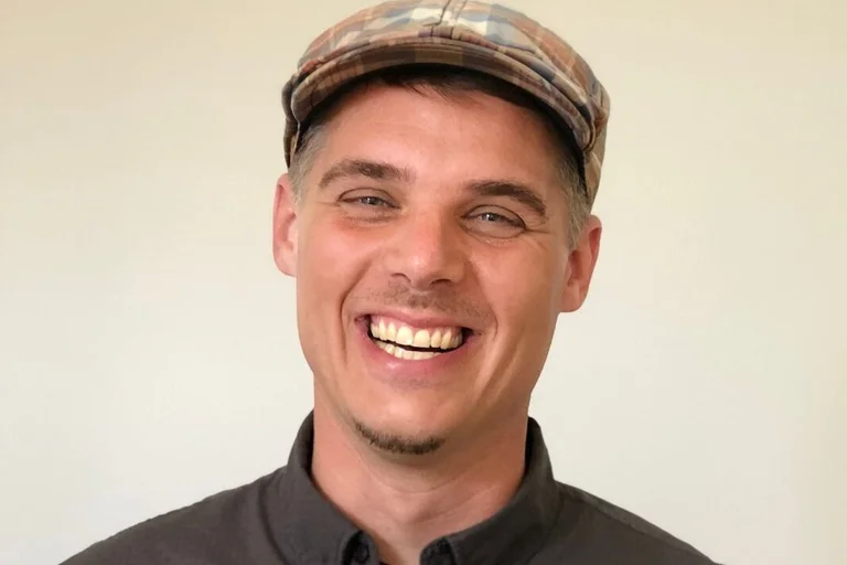 Ein junger Mann mit modischer karierter Mütze lacht herzlich in die Kamera