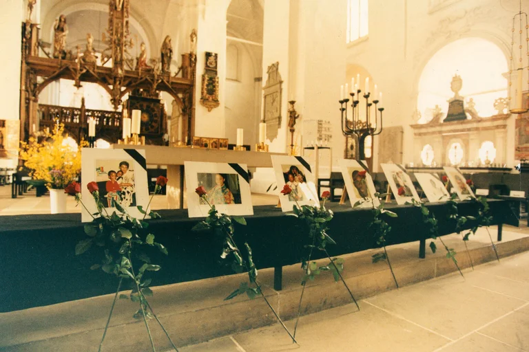 Blick in eine Kirche, in der Bilderrahmen mit Fotos und mit einer Rose aufgestellt sind