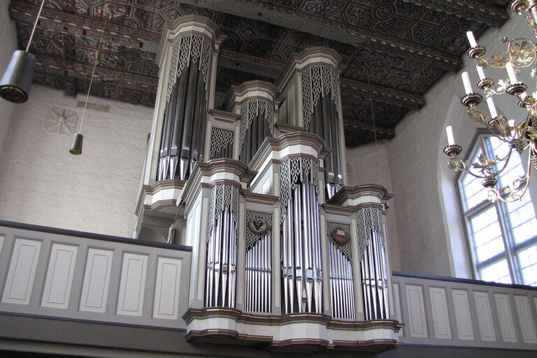 Eine alte weiße Orgel auf einer weißen Empore in einer Kirche. Die Holzdecke ist verziert.
