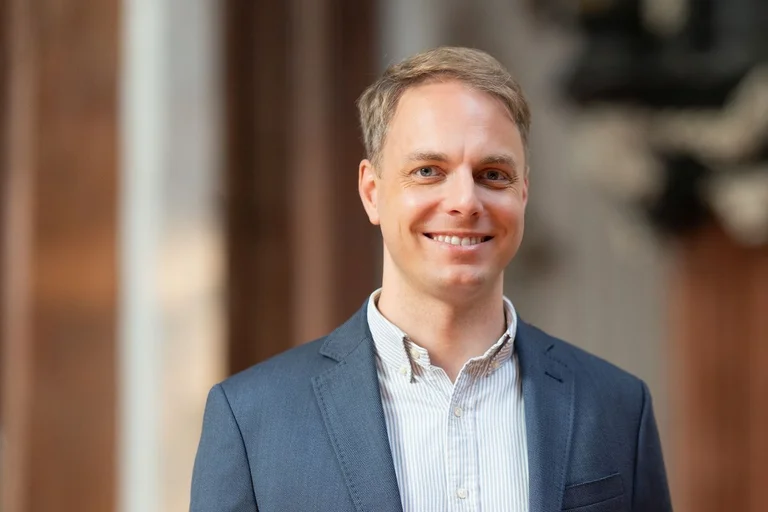 Ein Man mit blauem Sacko und kurzen blonden Haaren lächelt in die Kamera.