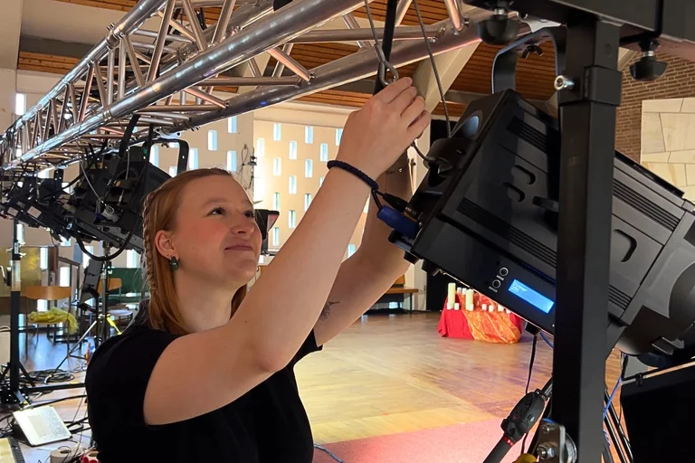 Eine junge Frau arbeitet an einem großen Scheinwerfer.