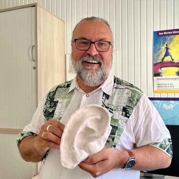 Mann steht mit Gipsohr in der Hand da und lächelt in die Kamera.