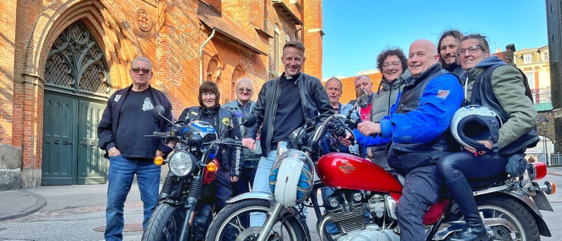 Eine Gruppe Menschen stehen mit zwei Motorrädern vor einer Kirche. 