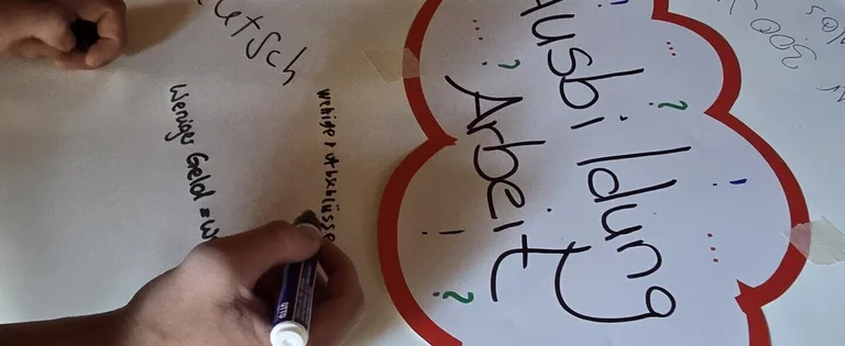 Hände schreiben Stichwörter zum Thema Ausbildung und Arbeit auf ein großes Blatt.